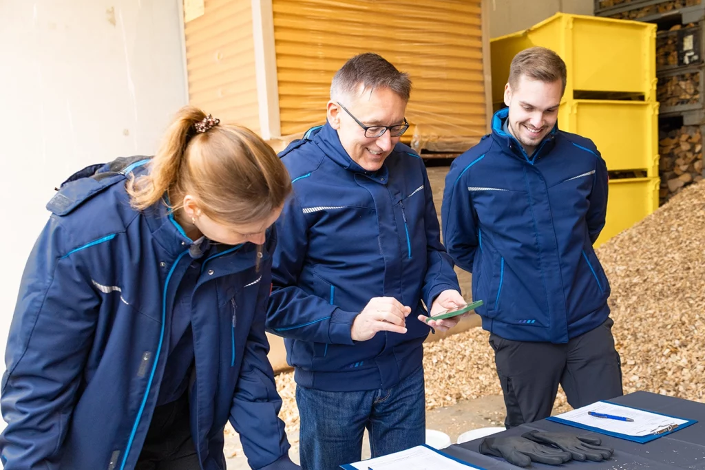 Drei Mitarbeiter der Technologica GmbH nehmen zusammen eine Probe von Altholz und lachen dabei.